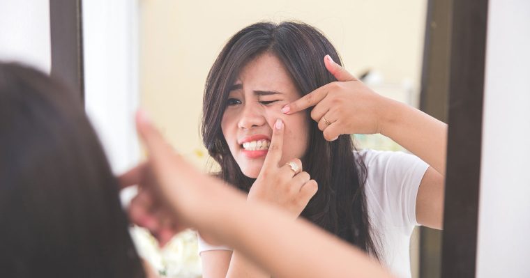 girl pressing pimple in front of a mirror